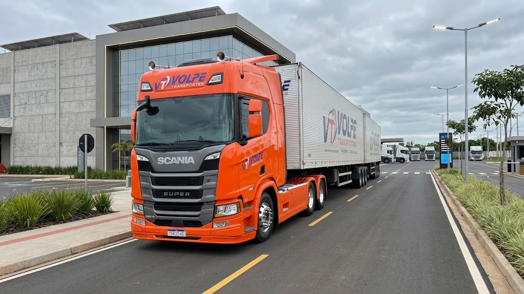 Caminhão laranja da Volpe Transportes diante de estrutura logística moderna
